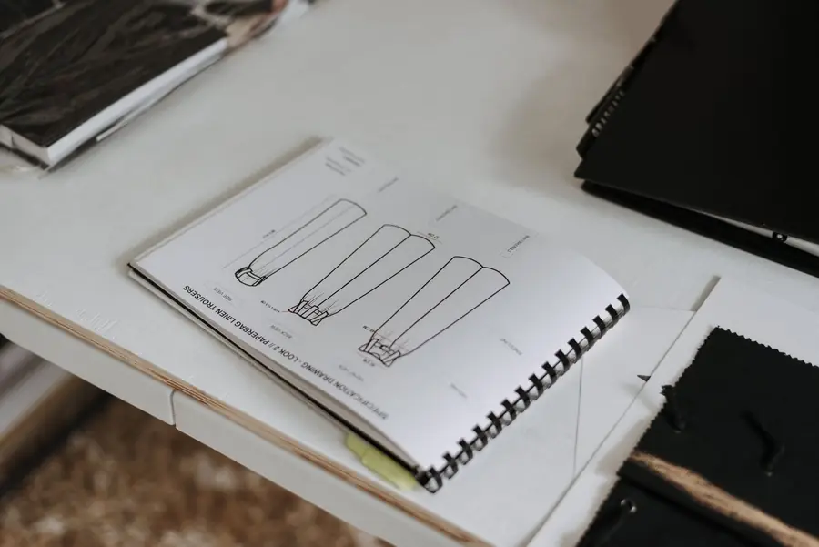 From above of sketchbook with sketches of new collection of clothes placed on white table in modern light professional studio with various folders